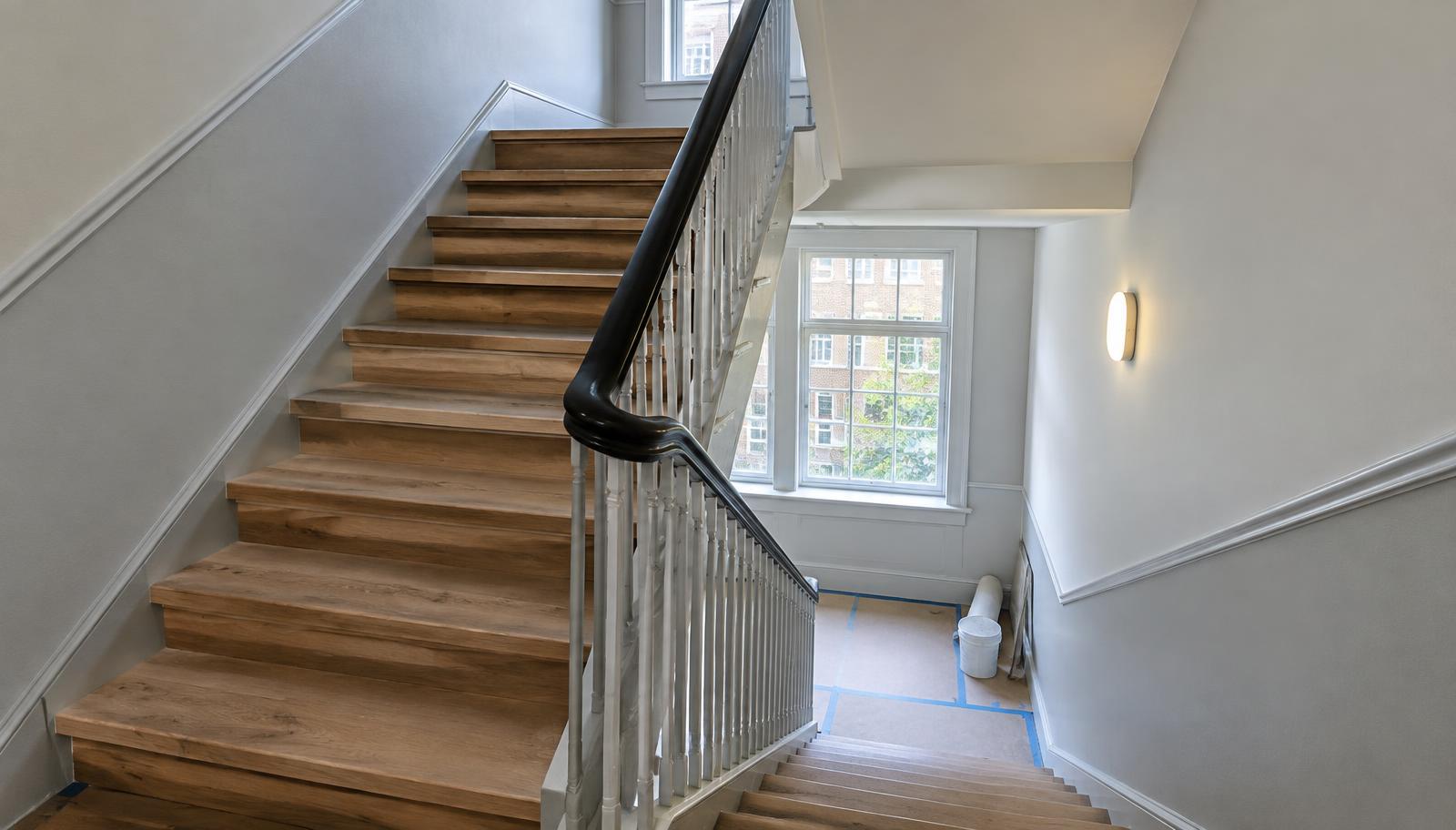 Istandsatte trætrin, gelænder og nymalede vægge i en trappeopgang under renovering