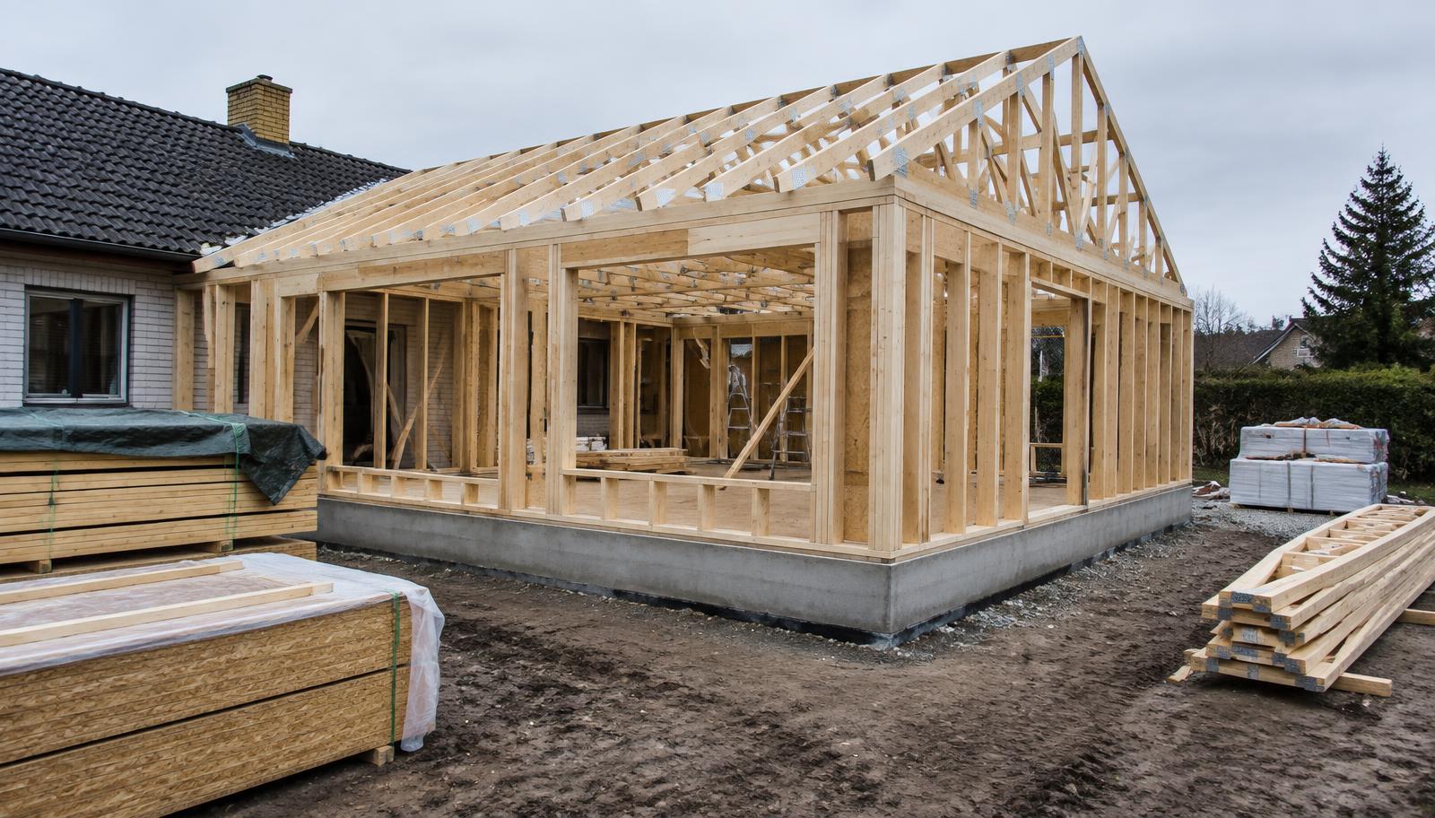 Tilbygning under opførelse med træskelet og spær rejst på nystøbt fundament
